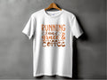 A stylish Garment Graphics T-shirt hangs on a gray wall, displaying the motivational phrase Running on grace & coffee in elegant brown lettering.