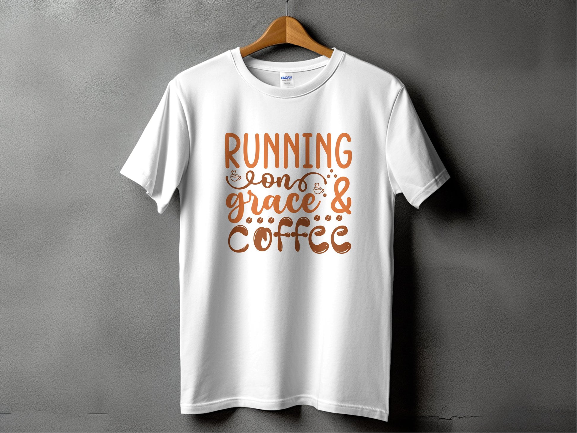 A stylish Garment Graphics T-shirt hangs on a gray wall, displaying the motivational phrase Running on grace & coffee in elegant brown lettering.