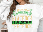 A person wears a white Garment Graphics sweatshirt featuring a humorous graphic with the words If an Englishman gets run down by a truck, he apologizes to the truck in green, yellow, and tan. Available in unisex sizes.