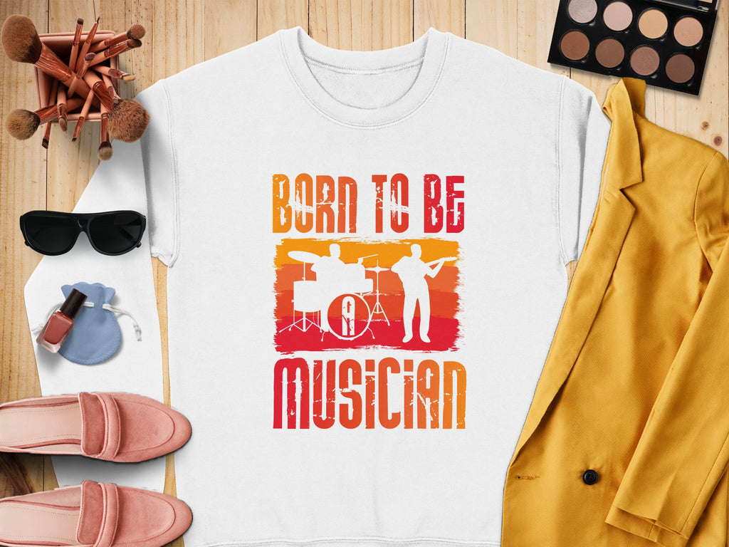 A white Garment Graphics t-shirt on wood showcases Born to be Musician with drummer and guitarist silhouettes, ideal for music lovers. Paired with a yellow jacket, makeup palette, brushes, sunglasses, pink shoes, nail polish, and a drawstring pouch. Unisex sizing is available.