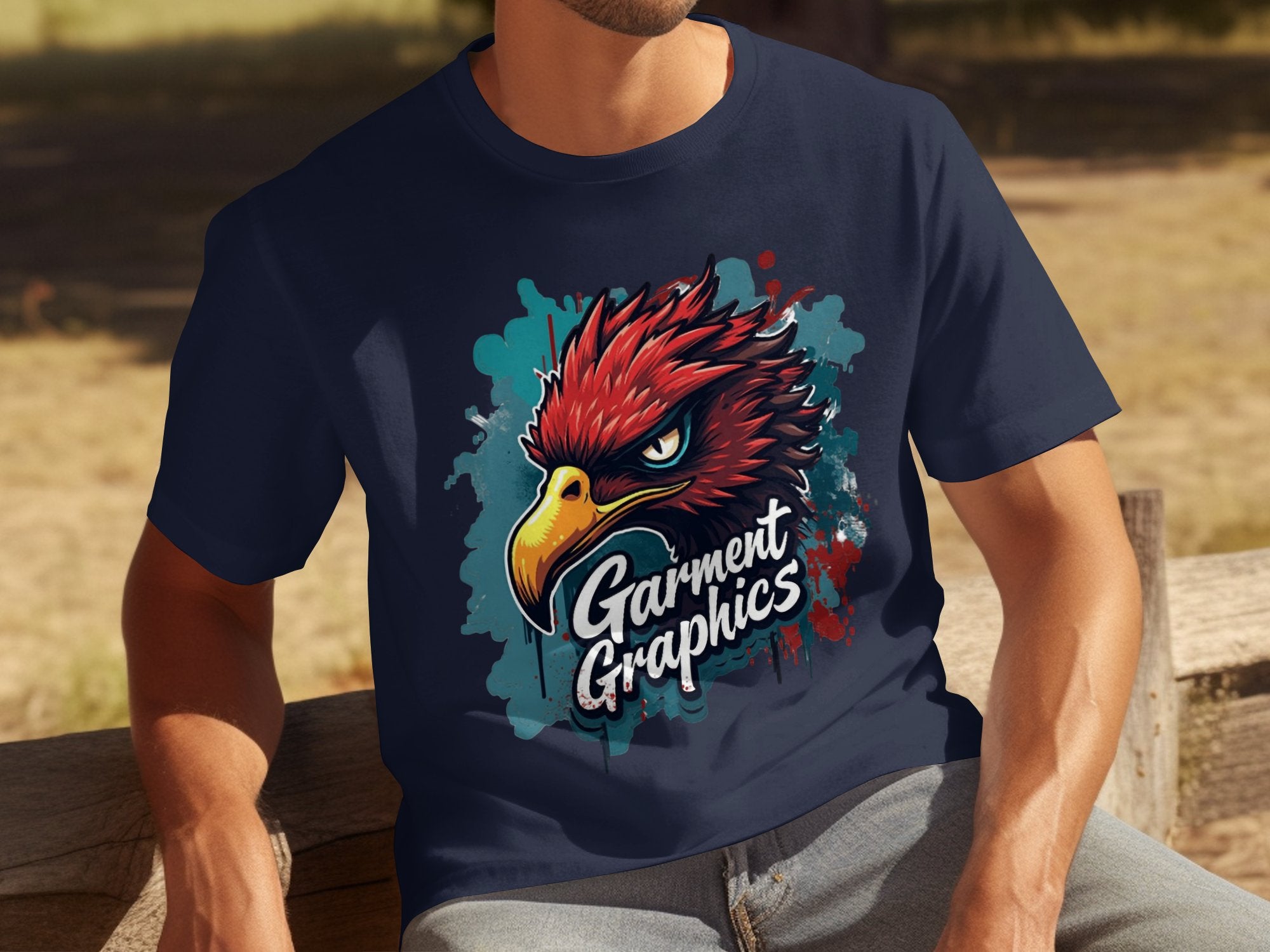 A person in a classic fit Garment Graphics navy T-shirt featuring an eagle design relaxes on a wooden bench outdoors, with grass and shaded areas in the background.