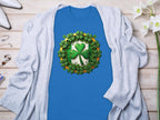 A Garment Graphics blue graphic T-shirt with a central shamrock clover and smaller shamrocks, paired with a light gray cardigan, creates a St. Patricks Day ensemble complemented by flowers, jewelry, and white shoes on a wooden surface.