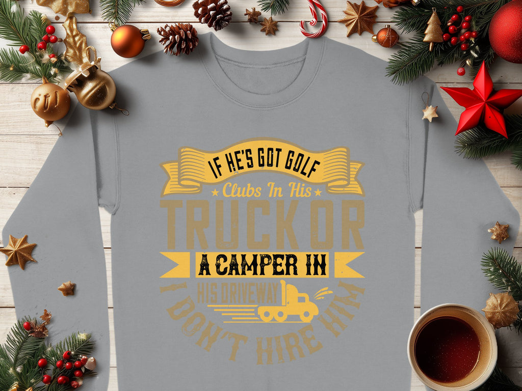 Garment Graphics offers a gray sweatshirt with the phrase If he’s got golf clubs in his truck or a camper in his driveway, dont hire him! in gold and yellow letters. Ideal for outdoor enthusiasts, its adorned with pine branches, ornaments, and coffee on a wooden table.