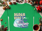 The Garment Graphics green shirt has a retro roadtrip graphic featuring a vintage car, surfboard, wave, and palm trees with Beach Vibes text. Showcased with Christmas decor on wood, it includes ornaments, pine cones, and coffee. Available in unisex sizing for comfort.