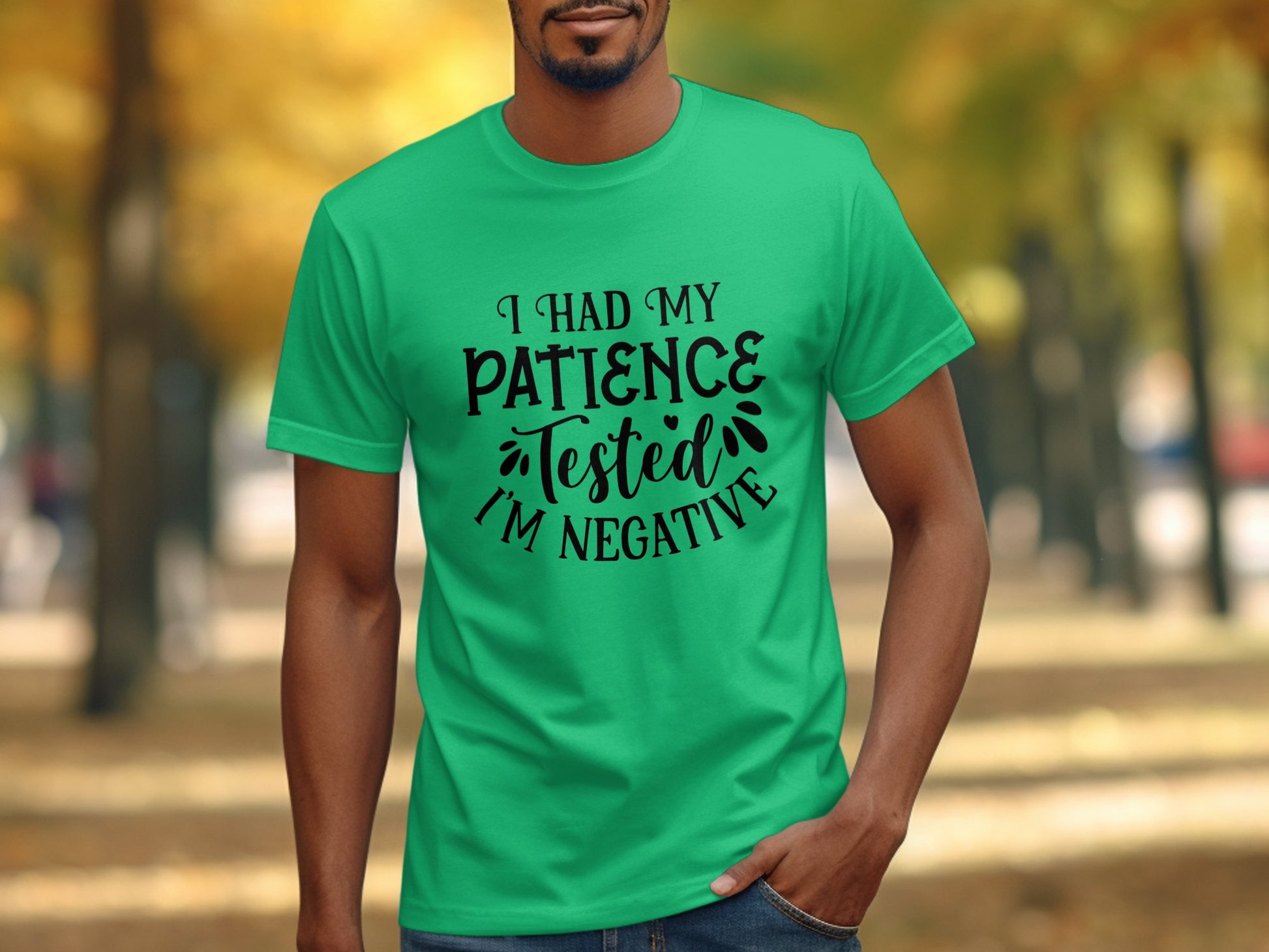 A man with a sarcastic attitude wears a humorous Garment Graphics T-shirt reading I Had My Patience Tested, Im Negative. He stands outdoors with blurred trees in the background.