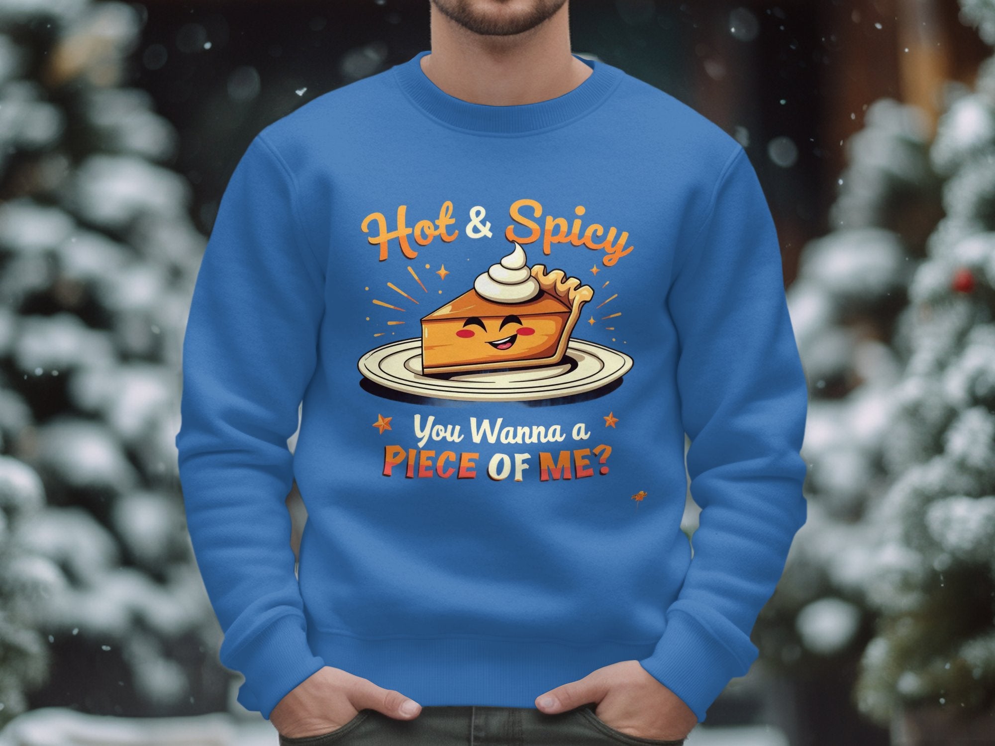 A person wears a Garment Graphics blue sweatshirt with a playful pie character topped with whipped cream. The text reads Hot & Spicy above and You wanna piece of me? below. This design stands out on the snowy background and is perfect for unisex sizing.