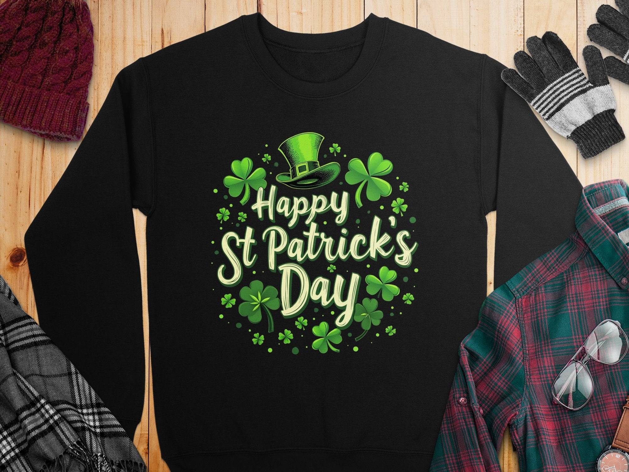 A black Garment Graphics shamrock sweatshirt with Happy St Patricks Day in green font is stylishly displayed on wood, perfectly paired with a maroon beanie, gloves, plaid shirt, and scarf for a festive look.