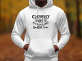 A person wears a white hoodie from Garment Graphics Cleverly Disguised Hoodies collection, featuring Cleverly disguised as a responsible adult in bold black text, set against a blurred outdoor background rich in autumn colors, embodying the essence of casual wear hoodies.