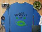 Garment Graphics blue sweatshirt, featuring Happy St. Patricks Day text and green lips graphic, captures the festive clover kiss spirit, displayed among a camera, lens, kiwi bowl, map, pouch, and closed notebook on a wooden surface.