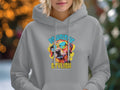 A person in a light gray hoodie from Garment Graphics, featuring a colorful dog wearing sunglasses design and the text PAWSITIVE STYLISH, stands out against a softly blurred background with circular lights, highlighting this vibrant and unique style.