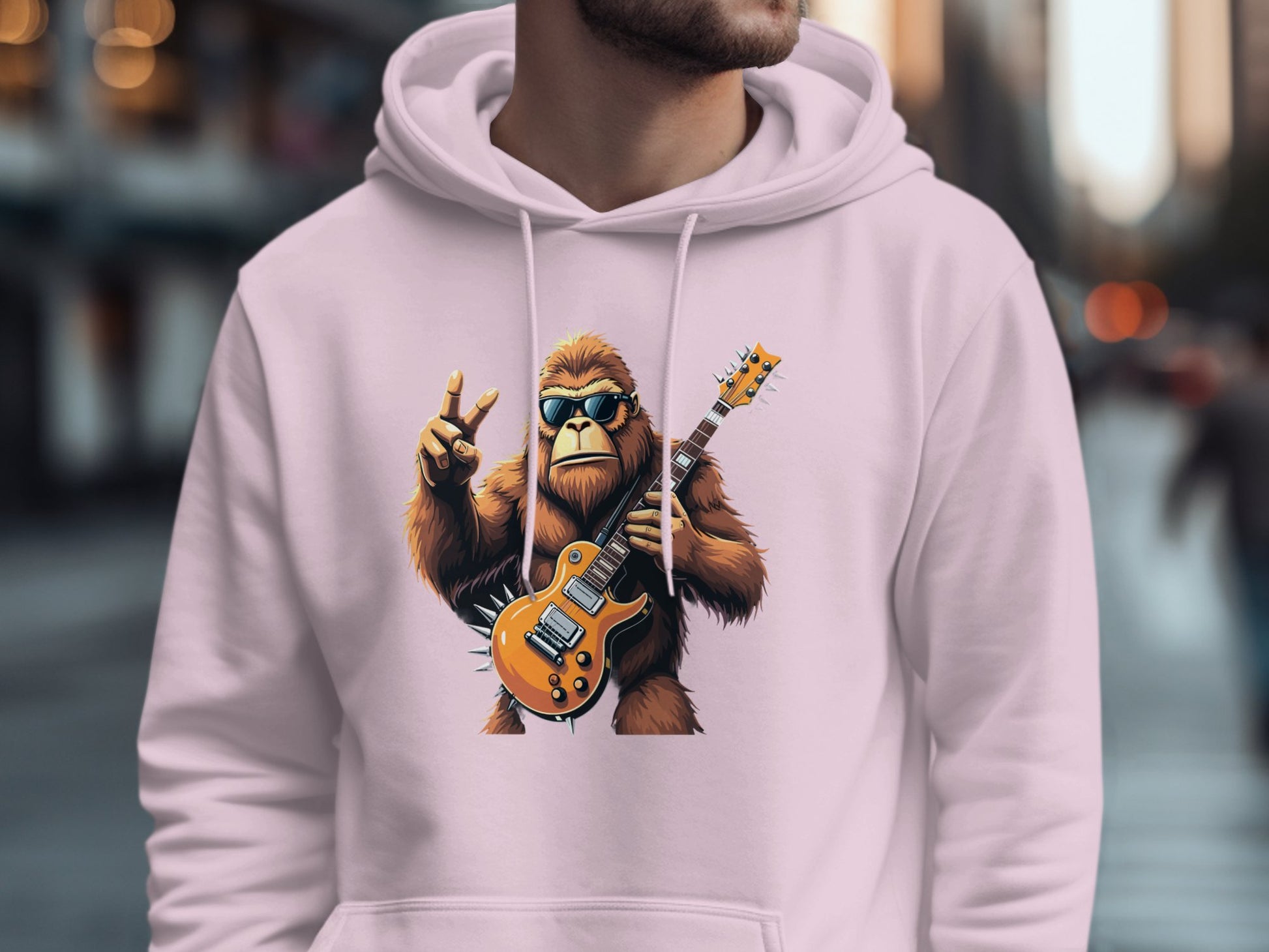 A person wearing a Garment Graphics light pink hoodie with a guitar-playing gorilla in sunglasses making a peace sign. Ideal for music lovers, it features a blurred street scene in the background.