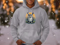 A person in a gray Garment Graphics hoodie, featuring a vibrant fierce owl illustration with feathers on a branch and an orange circle, stands in the snowy outdoors. Crafted from medium-heavy fabric, its perfect for chilly weather as snowflakes drift around.