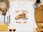 A unisex white sweatshirt from Garment Graphics features a playful pie graphic with a face and whipped cream crown, reading “Hot & Spicy” above and “You Wanna a Piece of Me?” below. Pair it with a scarf, notebook, pen, sunglasses, quilted jacket, or cup for a complete look.