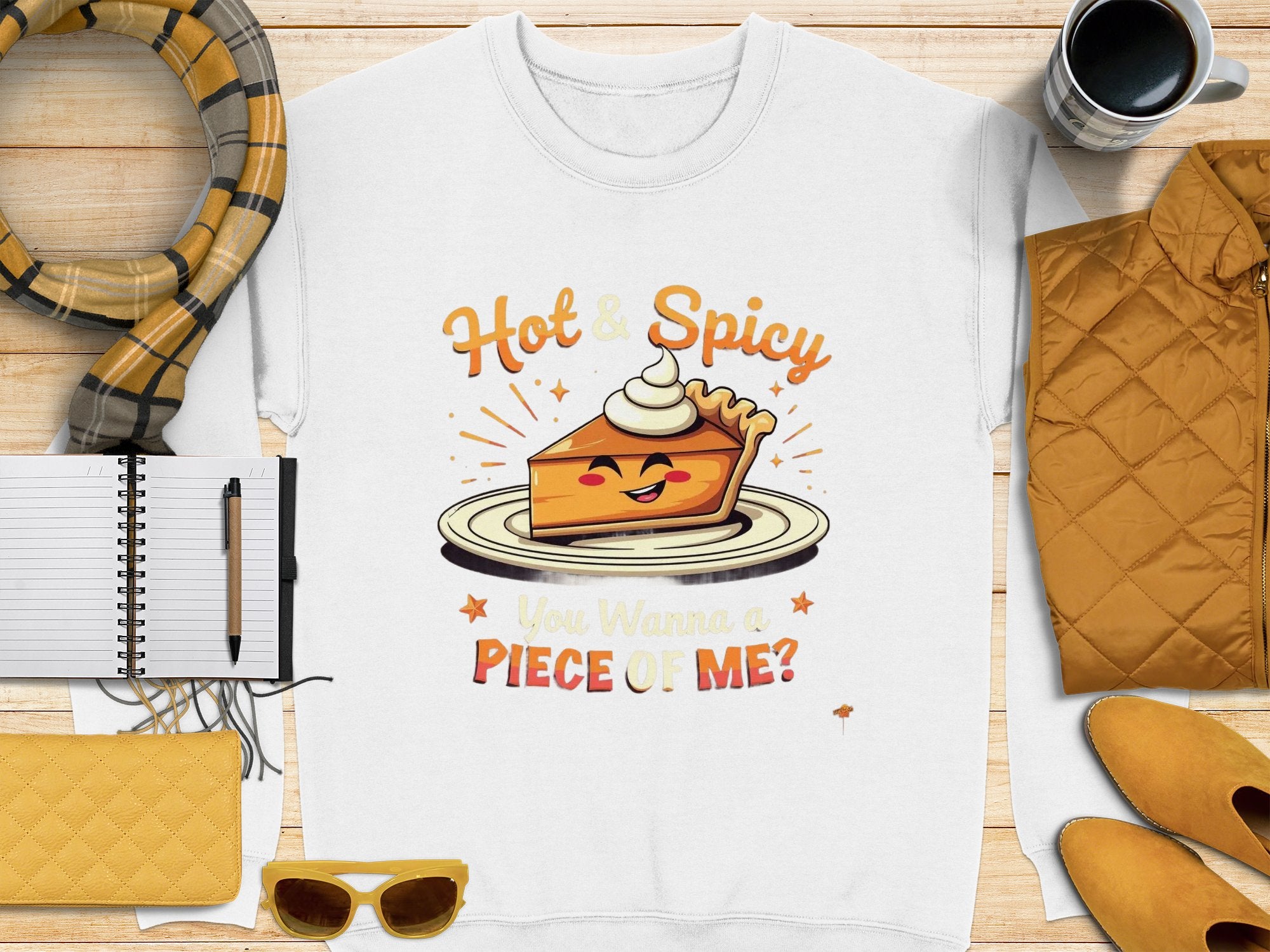 A unisex white sweatshirt from Garment Graphics features a playful pie graphic with a face and whipped cream crown, reading “Hot & Spicy” above and “You Wanna a Piece of Me?” below. Pair it with a scarf, notebook, pen, sunglasses, quilted jacket, or cup for a complete look.