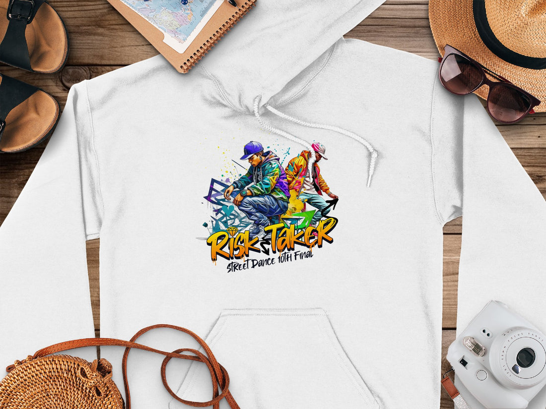 Garment Graphics presents a white hoodie featuring colorful dancer graphics and the phrase Risk Taker Street Dance. Accessories around it include a straw hat, sunglasses, camera, sandals, and notebook on a wooden surface.