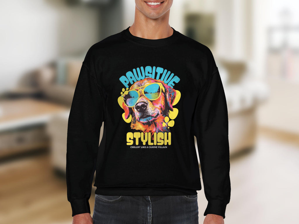 A person dons a black Garment Graphics sweatshirt with a vivid dog graphic wearing sunglasses and the phrase Pawsitive Stylish, ideal for dog lovers, against a softly blurred indoor background, emphasizing the sweatshirts trendy appeal.
