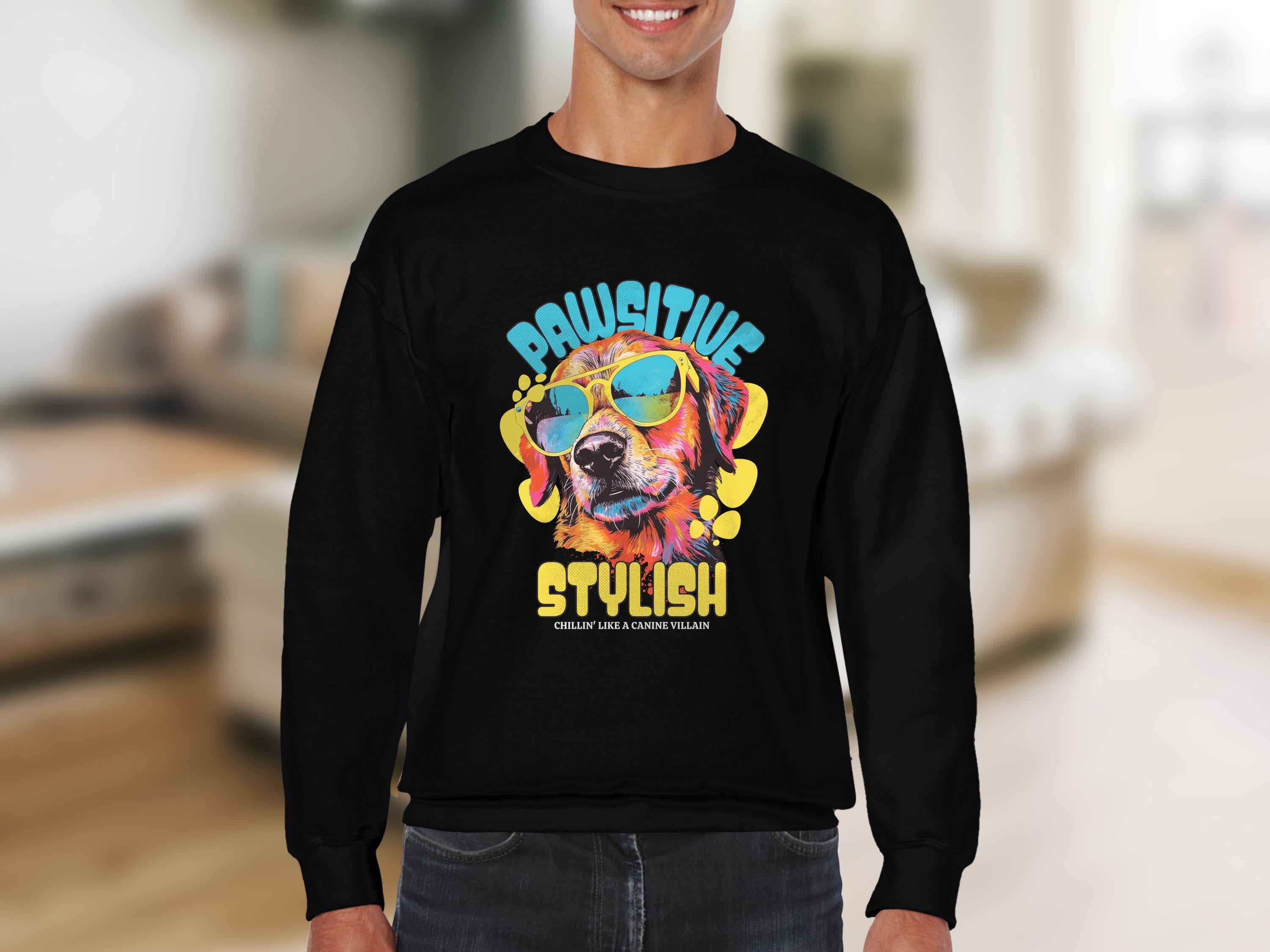 A person dons a black Garment Graphics sweatshirt with a vivid dog graphic wearing sunglasses and the phrase Pawsitive Stylish, ideal for dog lovers, against a softly blurred indoor background, emphasizing the sweatshirts trendy appeal.