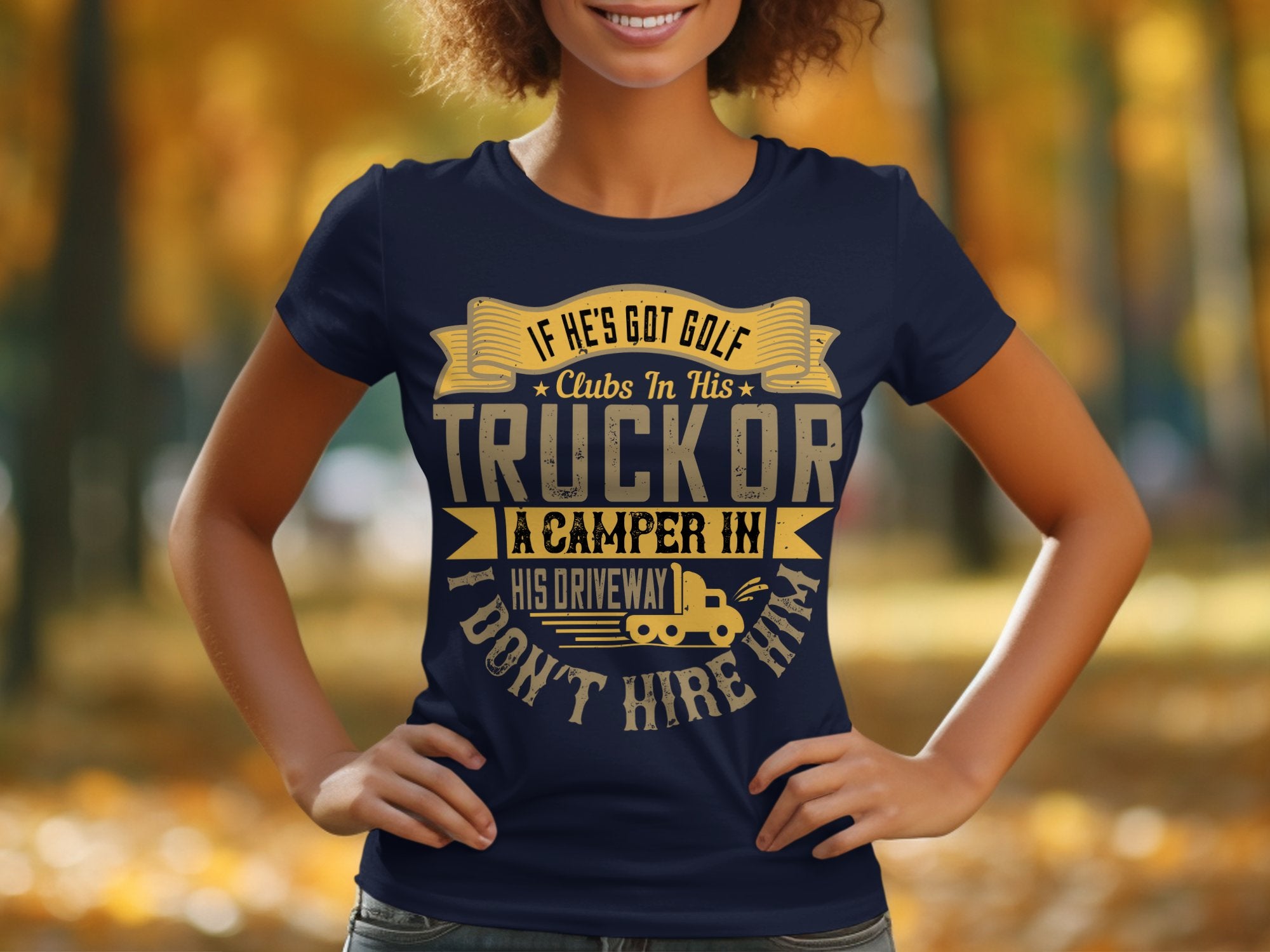 A person is wearing a quirky Garment Graphics navy blue T-shirt with gold lettering, If hes got golf clubs in his truck or a camper in his driveway, I dont hire him. This funny womens graphic tee features a backdrop of blurred autumn trees.