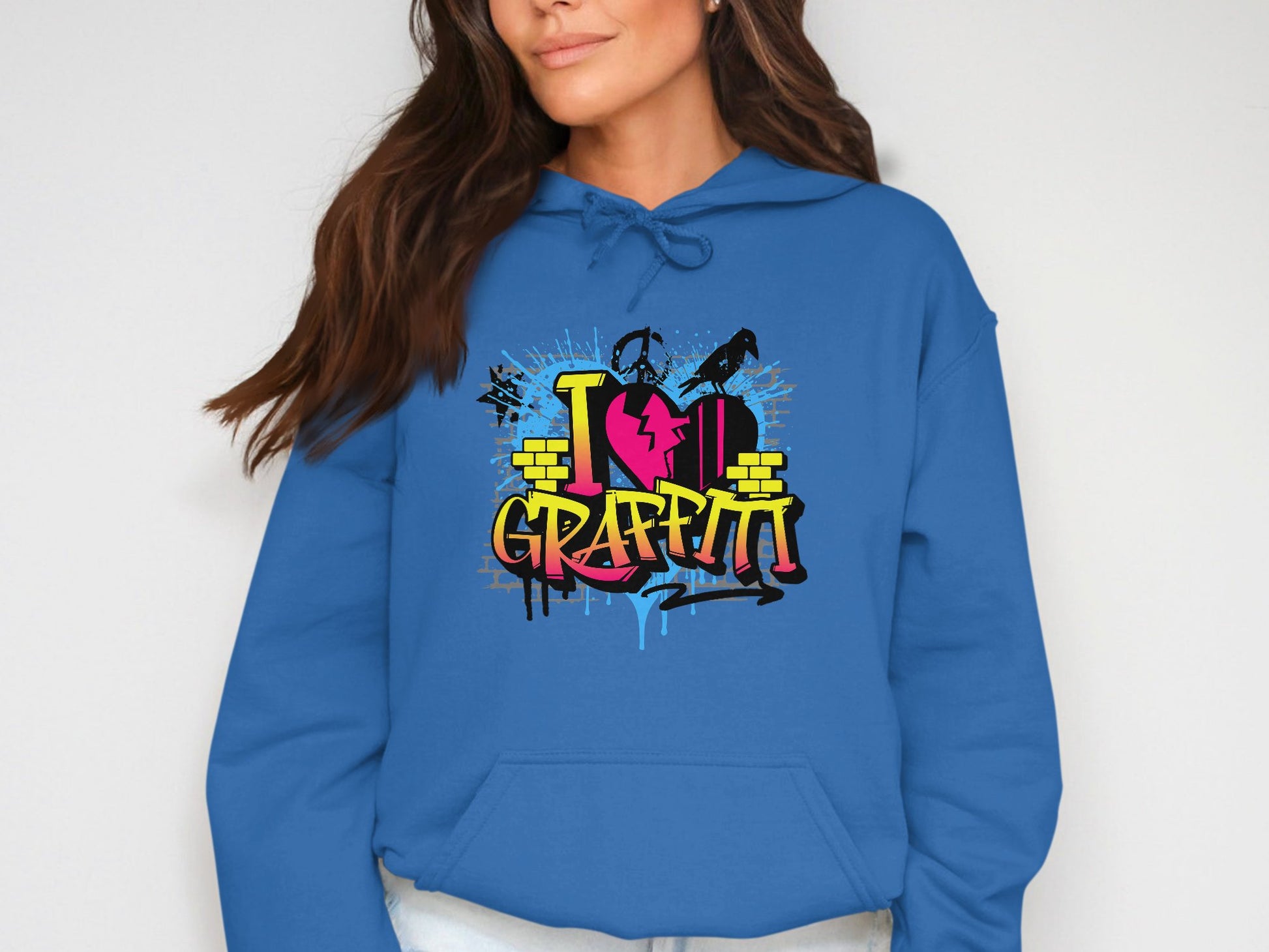 A person sports Garment Graphics blue hoodie adorned with a vibrant I Heart Graffiti design, ideal for casual wear. The graphic features urban street art elements like stylized text, paint splatters, and brick patterns. They have long brown hair and light skin, with their face partially out of view.