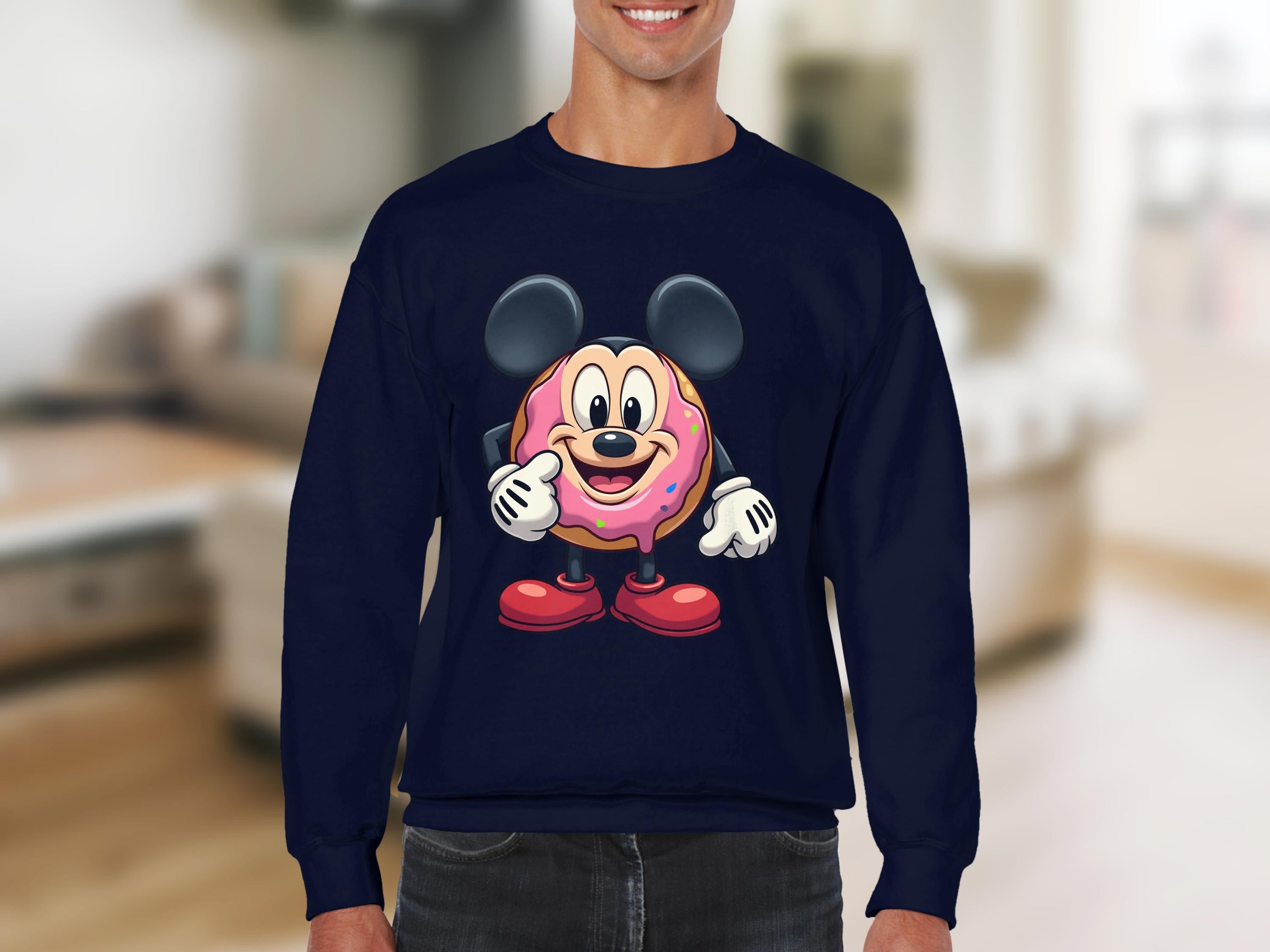 A person wears a Garment Graphics navy blue sweatshirt with a quirky donut character featuring large black ears, colorful detailing, big eyes, and gloves giving a thumbs-up. Available in unisex sizing, it stands out against the softly focused room backdrop.