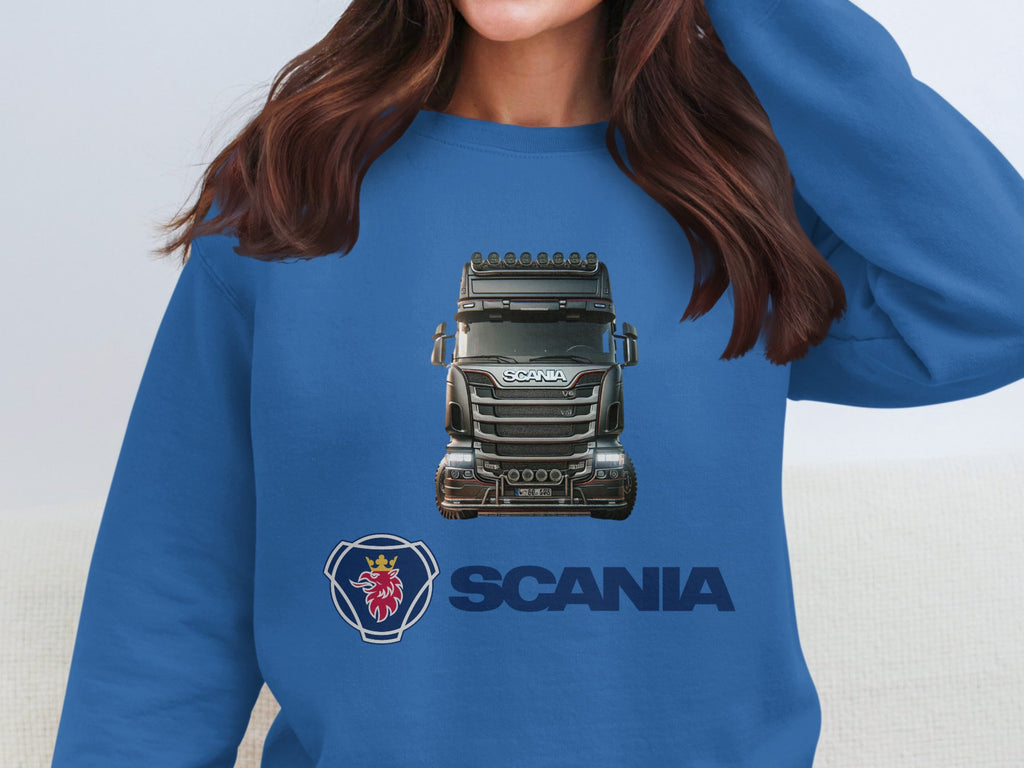 A person with long dark hair is wearing a Garment Graphics crewneck sweatshirt featuring a Scania truck graphic, prominently displaying the Scania logo and name. The persons face is not visible.