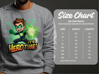 A person wearing a gray Garment Graphics sweatshirt featuring a colorful cartoon in a green superhero costume with glowing powers. The Its Hero Time! design graces the Gildan 18000 sweatshirt, ideal for adventure-loving youth. A size chart is available nearby.