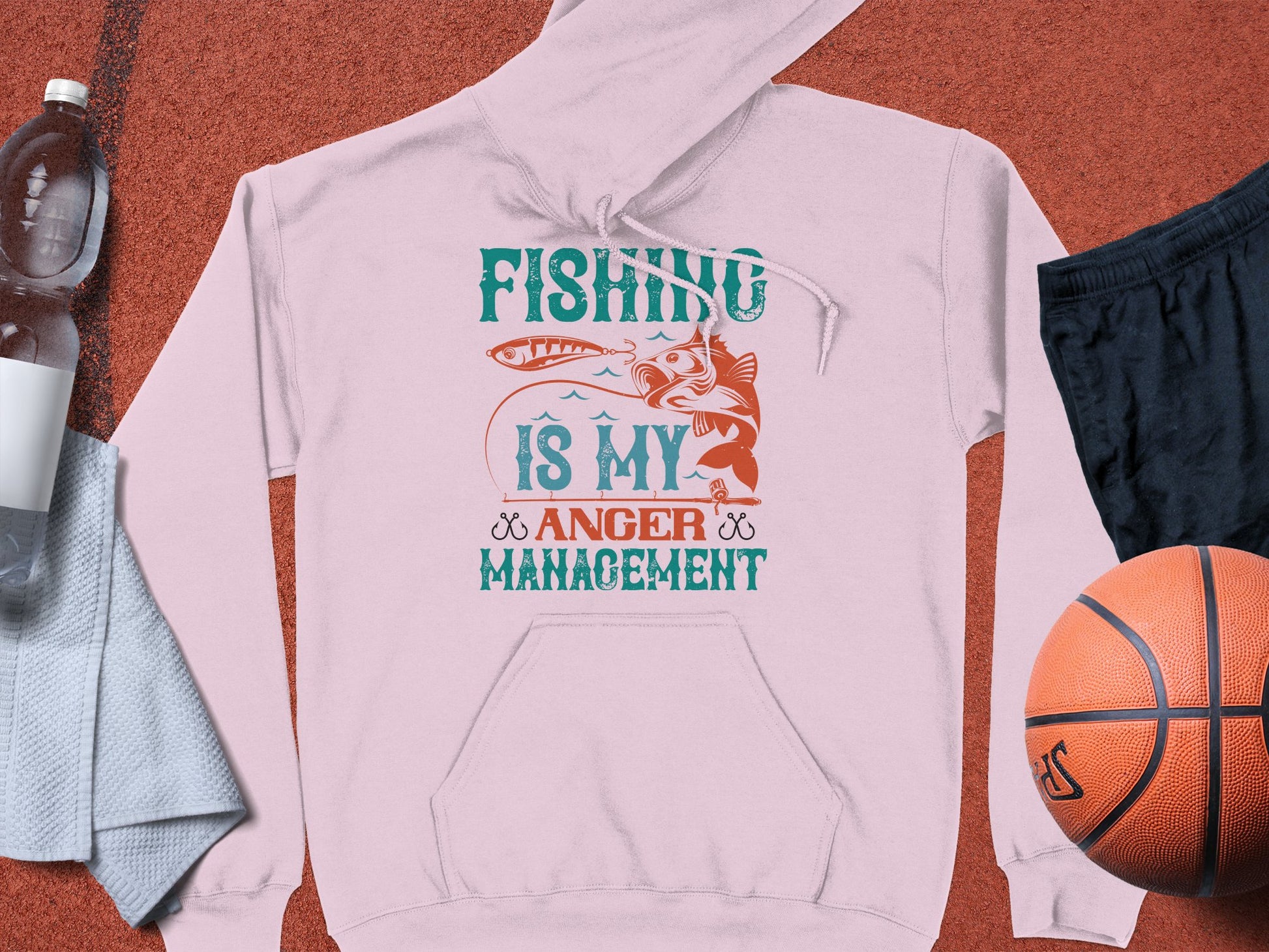 The Garment Graphics pink hoodie saying Fishing is my anger management, with a fish graphic, pairs well with a basketball, black shorts, a water bottle, and towel to enhance an anglers wardrobe.