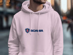 Wearing a trendy Garment Graphics white hoodie with the Scania logo and text, this person stands out in an urban street scene of blurred buildings and bustling crowds.