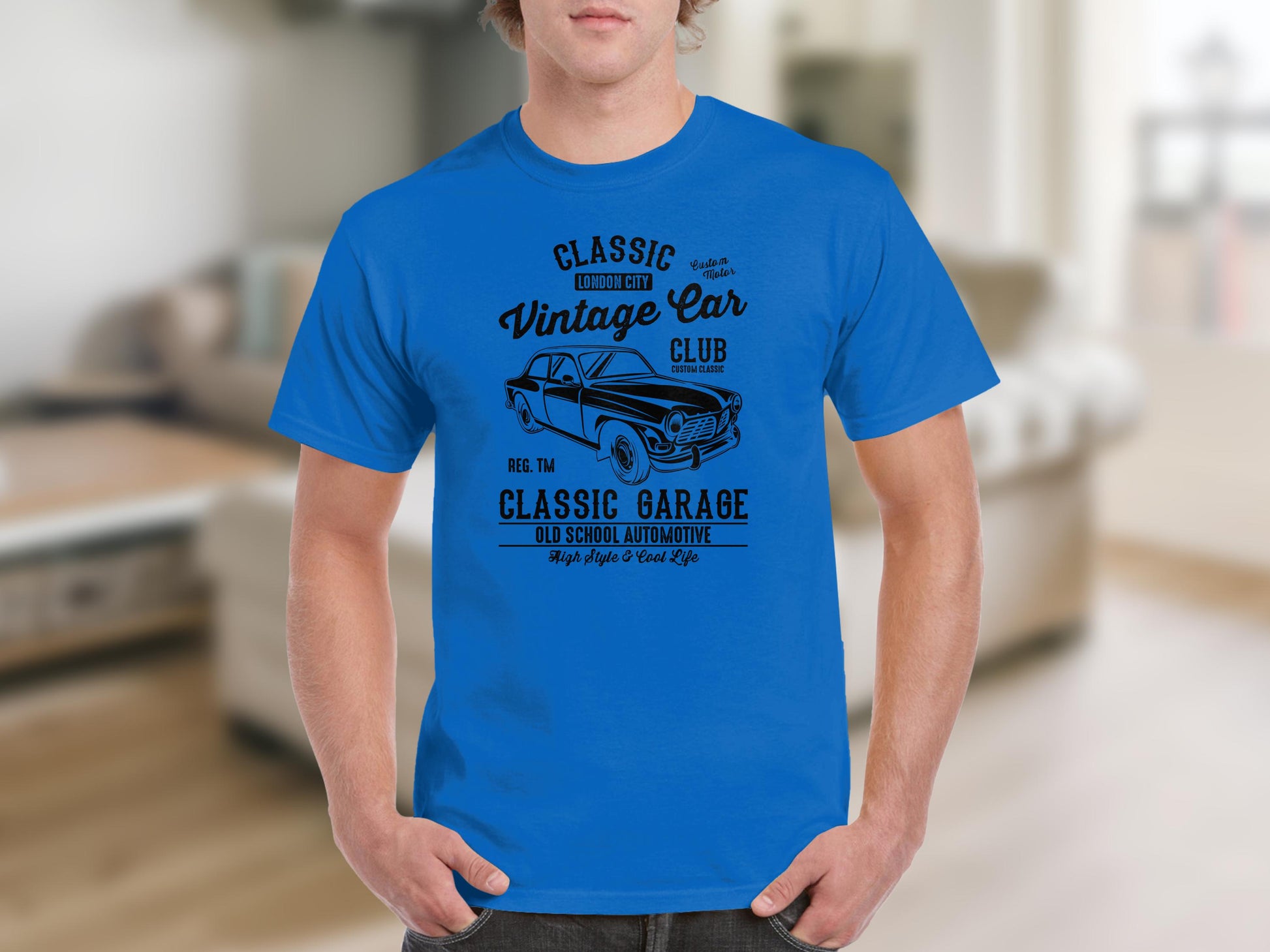 A person is wearing a blue Garment Graphics T-shirt in a classic fit, featuring black text and a vintage car design. The shirt reads Classic Vintage Car Club and Retro Automotive Old School, against a blurred indoor background.