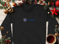 A black Garment Graphics hoodie with a blue Scania logo is displayed on wood, surrounded by festive pine cones, ornaments, stars, and a coffee cup—an exceptional fashion piece ideal for the seasons celebrations.