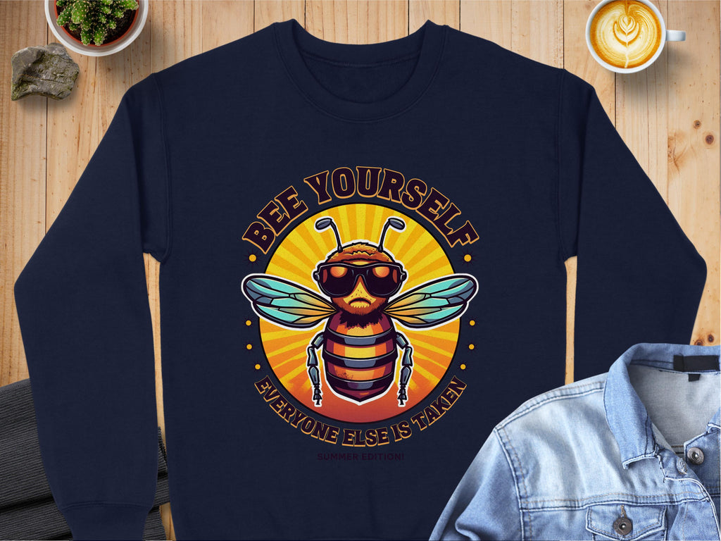 Garment Graphics presents a unisex navy blue summer edition sweatshirt showcasing a bee in sunglasses and headphones with the text Bee Yourself, Everyone Else is Taken on a sunburst backdrop. Its perfect for layering with a denim jacket while enjoying coffee and your plant collection.