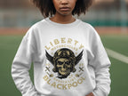 A person rocking a biker style with a white sweatshirt featuring a skull, wings, goggles, and Liberty Motorcycles Specialist Blackpool 2023 by Garment Graphics. The backdrop reveals a blurred outdoor setting.
