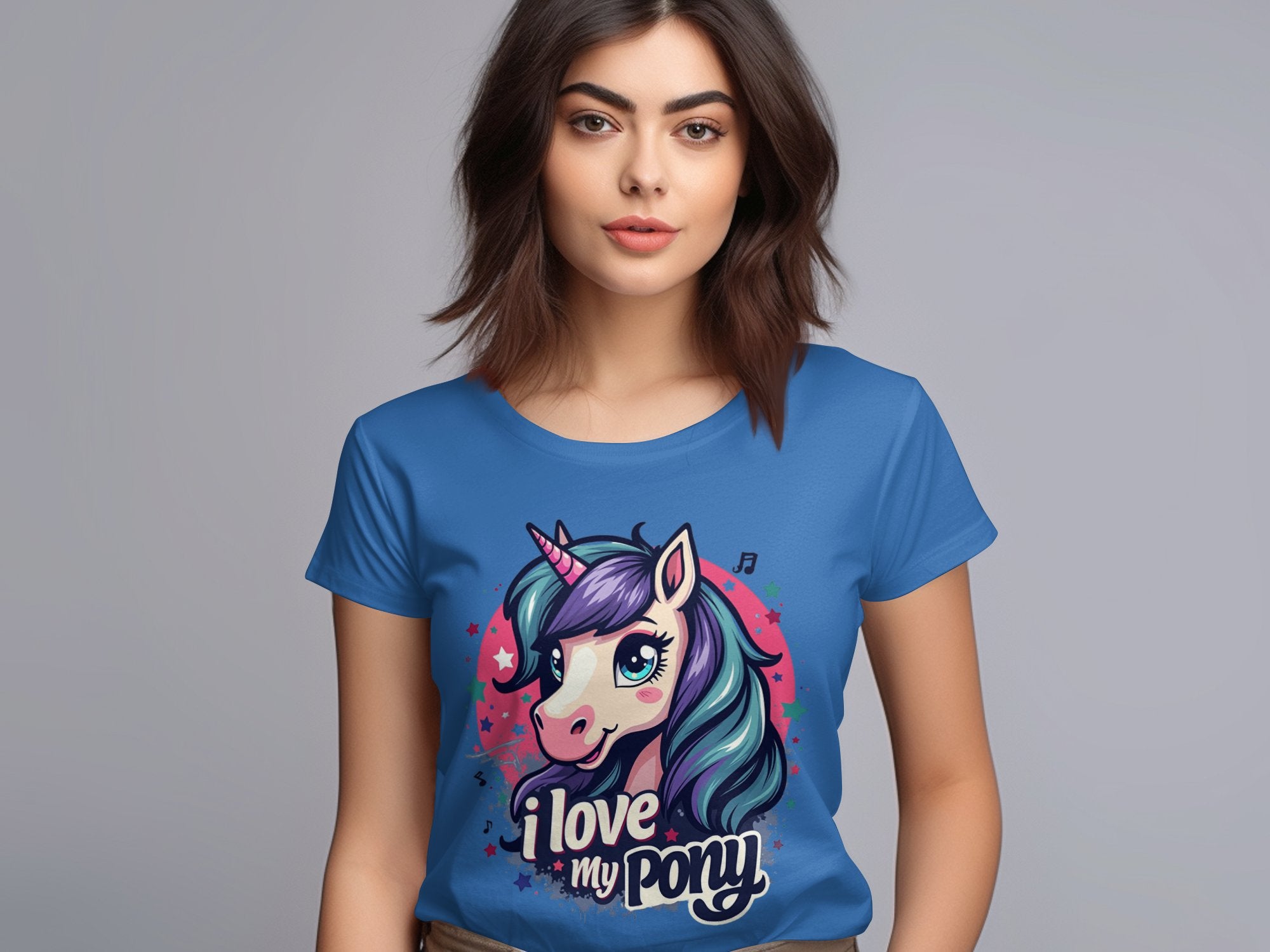 Against a plain gray backdrop, a unicorn enthusiast with long dark hair sports a Garment Graphics T-shirt featuring an I Love My Pony design with a vibrant unicorn graphic.