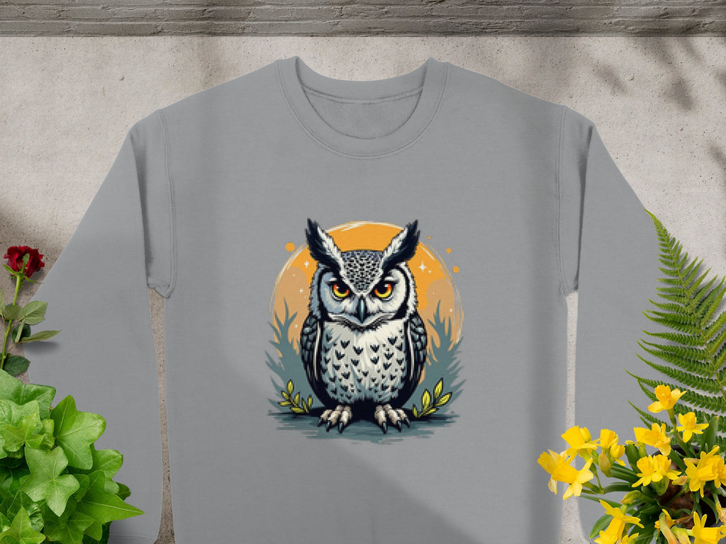 A gray sweatshirt from Garment Graphics showcases an intricate owl design with orange eyes within an orange circle, surrounded by foliage and yellow flowers. Available in unisex sizes for a perfect fit.