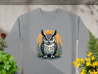 A gray sweatshirt from Garment Graphics showcases an intricate owl design with orange eyes within an orange circle, surrounded by foliage and yellow flowers. Available in unisex sizes for a perfect fit.