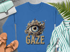 Garment Graphics blue sweatshirt features an ornate eye design labeled GAZE. It’s unisex and complements a striped shirt, brown sandals, a wristwatch, fern leaves, and a light blue bag on a gray surface.