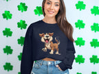 A woman in a Garment Graphics black sweatshirt with an animated happy dog illustration stands by a wall of green shamrocks. Her long brown hair flows over her shoulders as she smiles gently, creating an ideal scene for dog lovers.