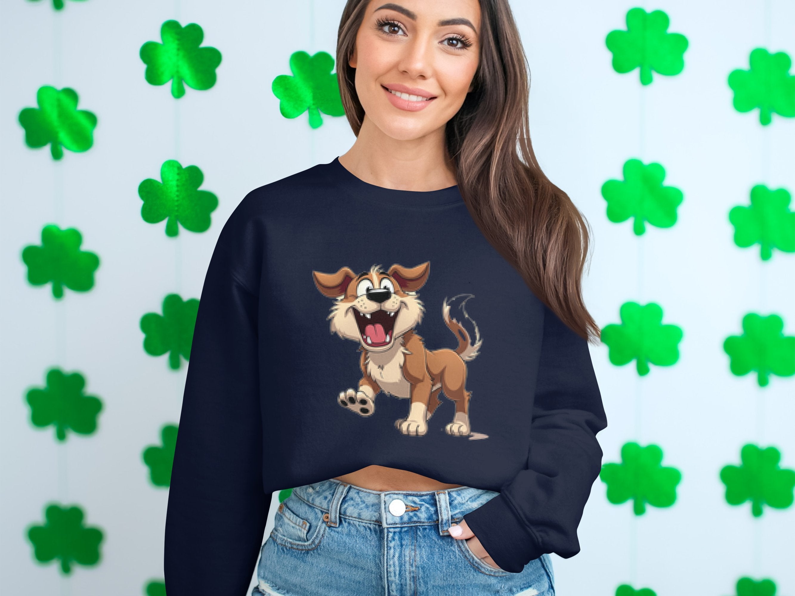A woman in a Garment Graphics black sweatshirt with an animated happy dog illustration stands by a wall of green shamrocks. Her long brown hair flows over her shoulders as she smiles gently, creating an ideal scene for dog lovers.