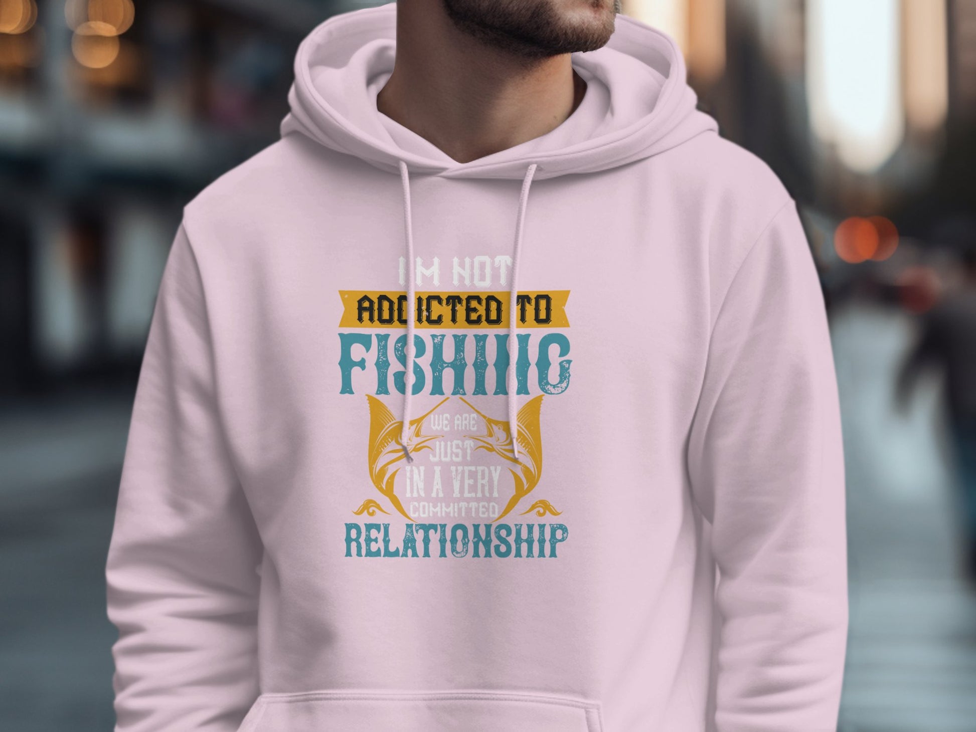 Someone is wearing a pink fishing hoodie from Garment Graphics, featuring the playful text: Im not addicted to fishing; we are just in a very committed relationship, creating a distinctive look against the blurred city street backdrop.