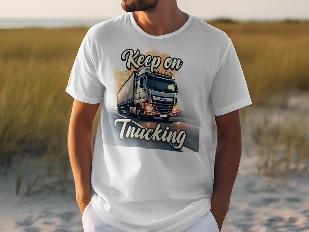 A truck enthusiast wears a Garment Graphics white t-shirt with a large truck graphic on a road, Keep on Trucking text, and a grassy field under a clear sky backdrop.