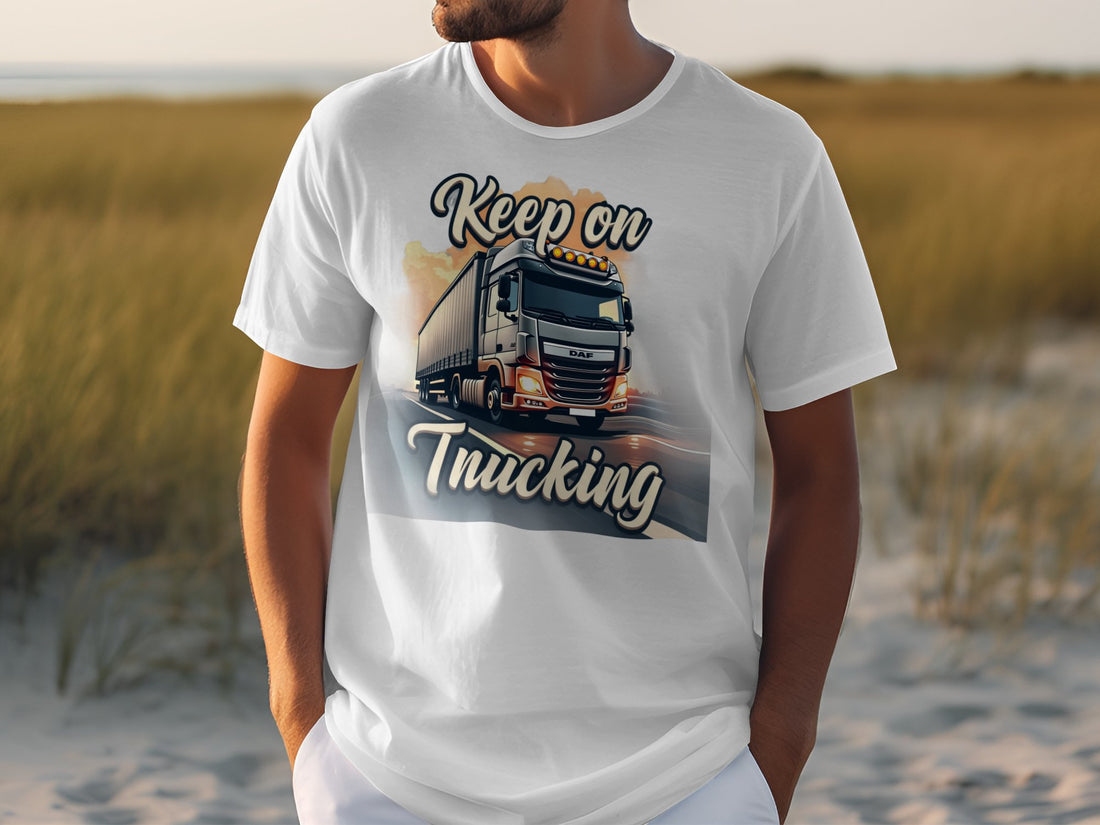 A truck enthusiast wears a Garment Graphics white t-shirt with a large truck graphic on a road, Keep on Trucking text, and a grassy field under a clear sky backdrop.