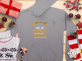 Garment Graphics gray hoodie features Father and Son, Fishing Partners for Life in yellow and white. Ideal for fishing fans, its displayed with Christmas items like wrapped gifts, a reindeer sweater, pine cones, candy, and stars on a wooden surface.