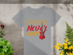 A Garment Graphics gray T-shirt with Music Never Sleeps in bold yellow and red letters and a striking red guitar motif lies surrounded by vibrant green plants and blooming yellow flowers.