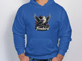 A person showcases a unique style in their blue Freebird Graphic Pullover Hoodie by Garment Graphics, featuring a birds outstretched wings above Freebird, with hands casually tucked into the front pocket.