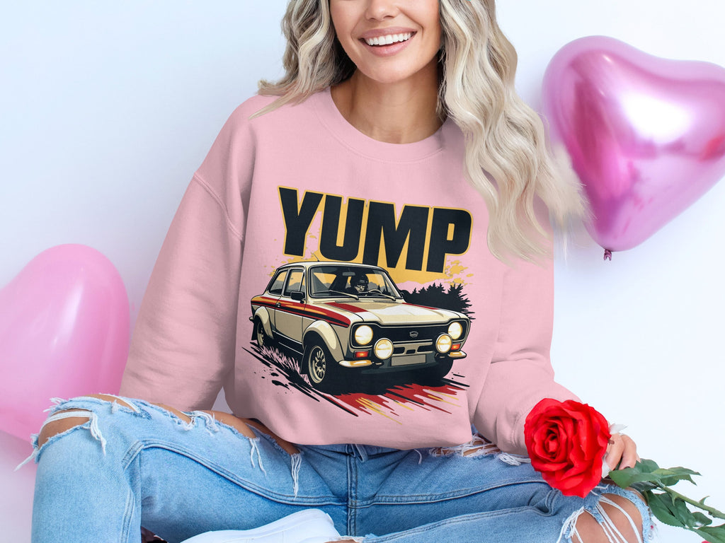 A person with long, wavy hair sits cross-legged, wearing a Garment Graphics pink sweatshirt with a rally car graphic. They hold a red rose next to metallic pink heart-shaped balloons and wear ripped blue jeans.