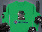 Garment Graphics green crewneck sweatshirt features a Scania trucks and logo design. Ideal for truck lovers, its styled alongside a smartphone, smartwatch, wireless earbud case, portable speaker, sneakers, and dumbbells on a gray surface.