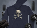 A fashion-forward dark hoodie featuring a skull and crossbones design by Garment Graphics takes center stage. Its surrounded by a smartphone, smartwatch, wireless speaker, dumbbells, and sleek black sneakers on a polished gray surface.