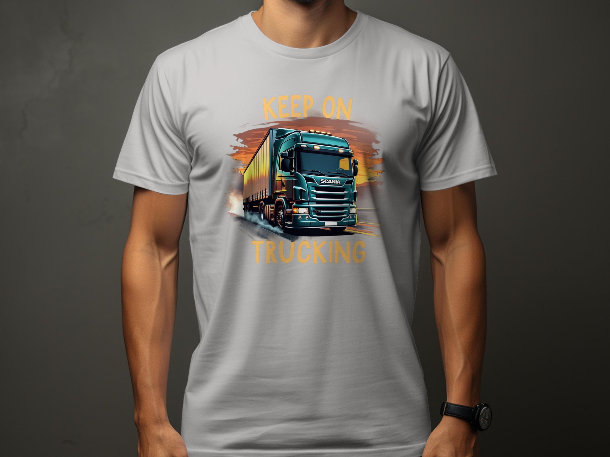 A truck enthusiast wears a Garment Graphics light gray T-shirt featuring a large truck graphic and the bold text KEEP ON TRUCKING on the front, set against a solid dark background.