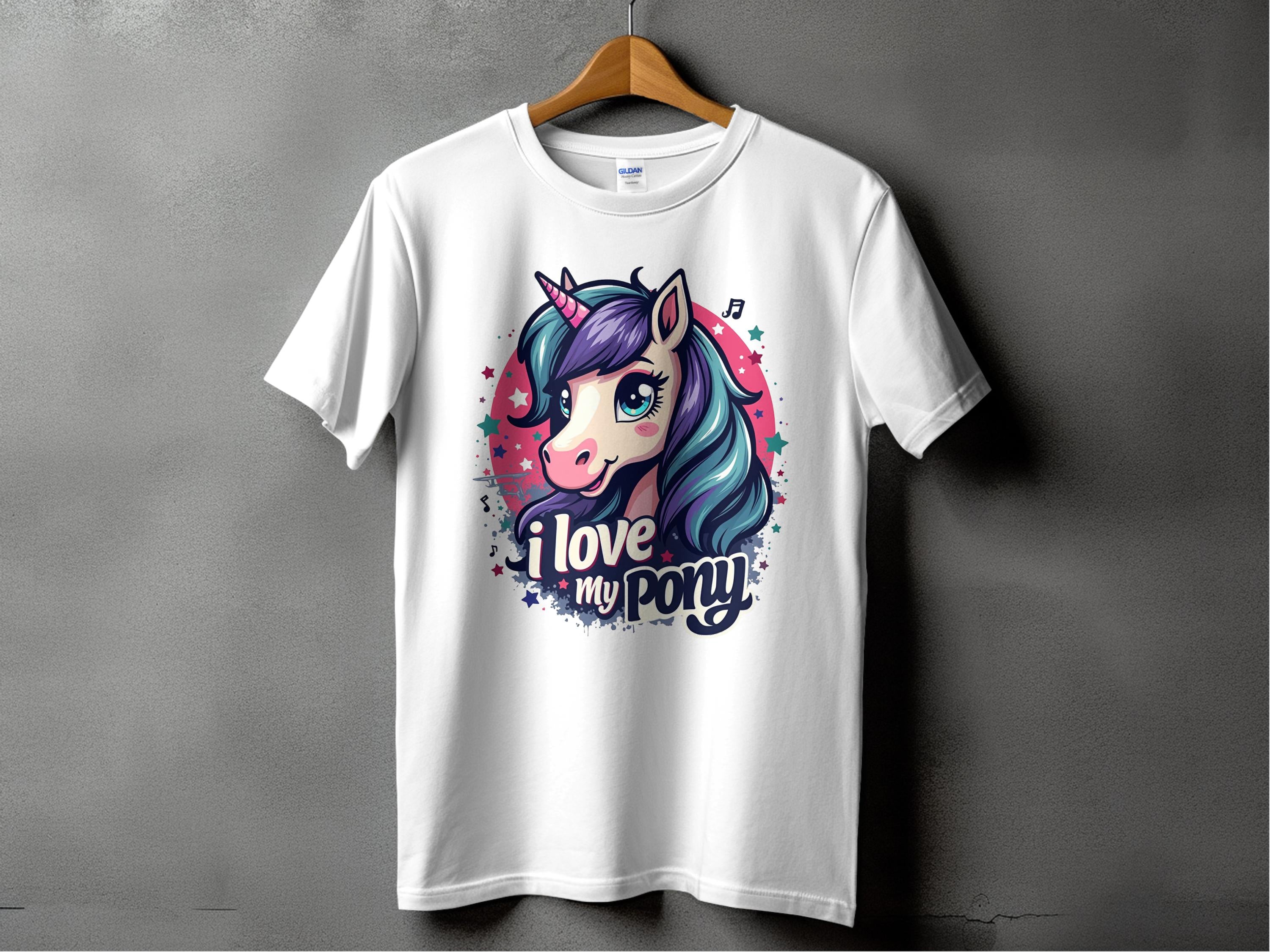 A Garment Graphics T-shirt in white hangs on a wooden hanger against a gray backdrop, featuring a cartoon pony with a vibrant mane and unicorn horn, surrounded by stars. The playful text says, I love my pony, ideal for any unicorn fan.