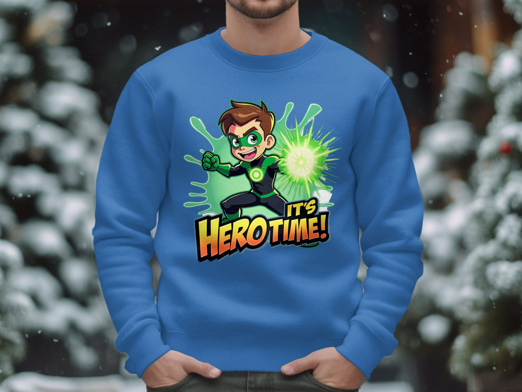 A person is wearing a Garment Graphics blue sweatshirt with a colorful animated character in a green costume holding a glowing orb. The phrase Its Herotime captures the adventure-loving spirit, set against blurred snowy trees in the background.